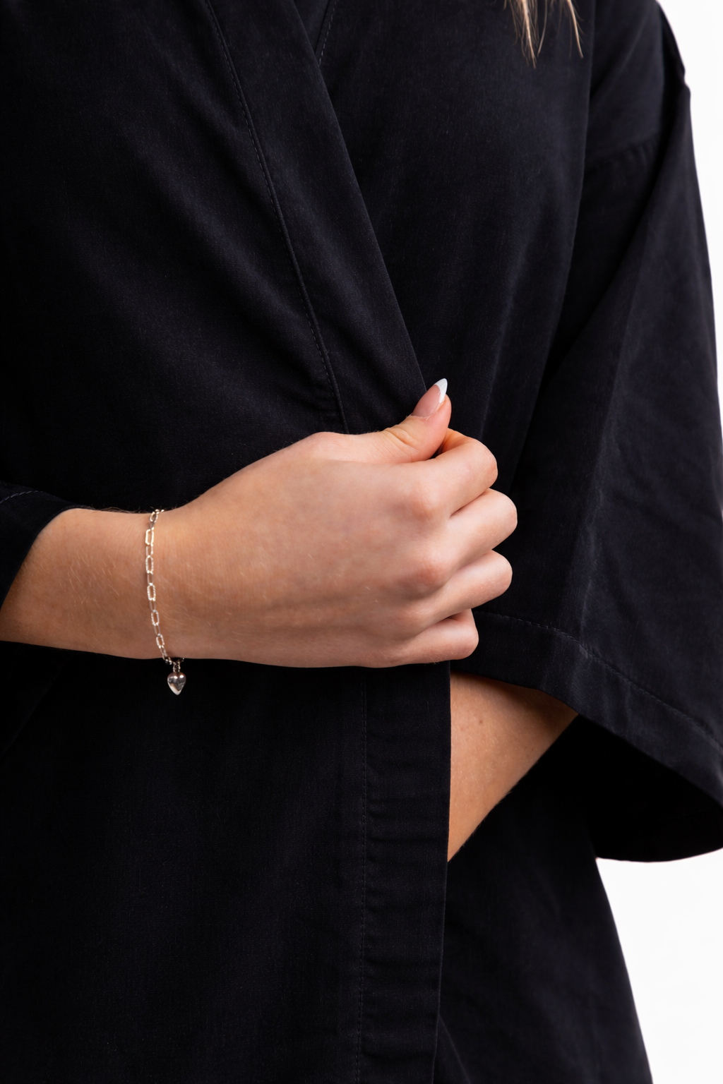 A close-up view of a person's hand holding the lapel of a black salon robe, showing a silver chain-link bracelet with a small heart charm.