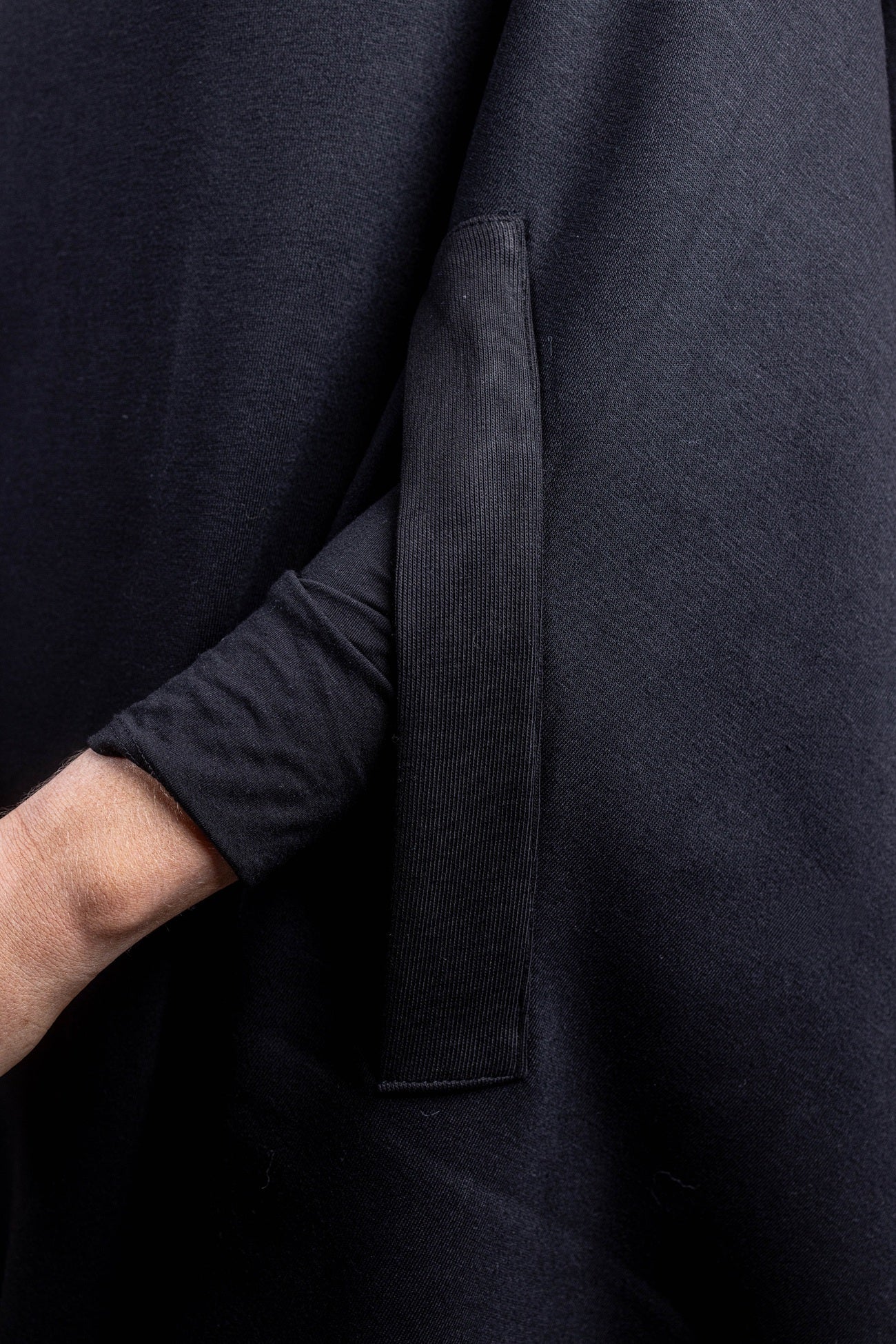 A close-up detail shot of a black salon cape, highlighting the vertical integrated arm slit that allows for client mobility and arm access through the fabric.