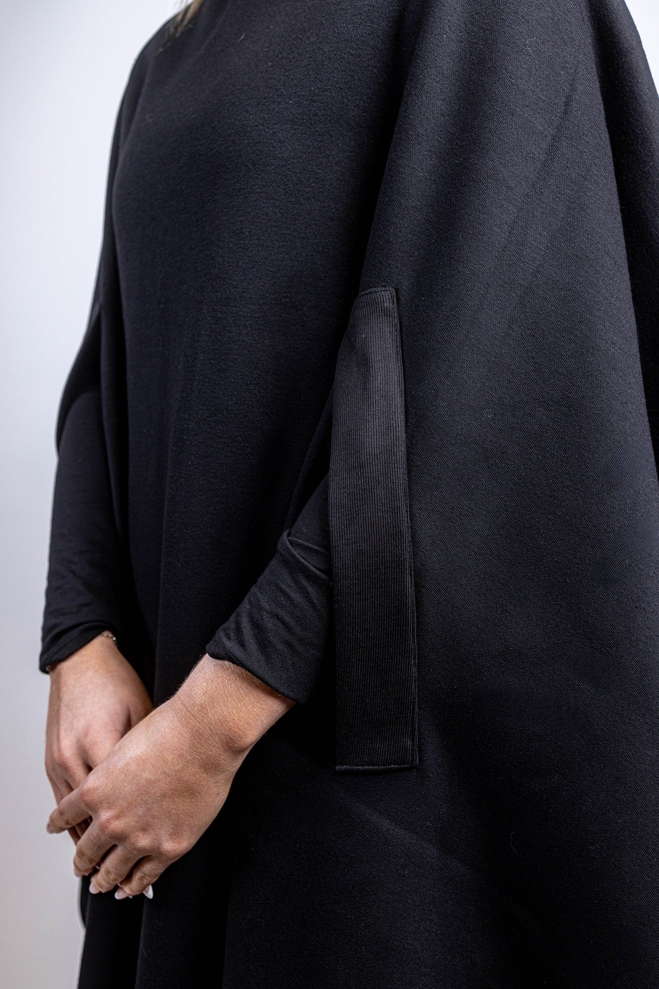 A side profile view focusing on the integrated arm slit of a black salon cape, showing a person's arm emerging through the functional opening in the fabric.