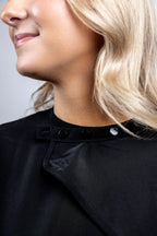 A close-up detail shot focusing on the black snap-button neck closure of a professional black salon cape, showing the secure and adjustable fasteners.