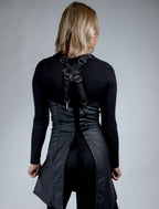 A rear-view photograph of a stylist wearing a black sweetheart neckline apron from The Branded Salon, showcasing the adjustable cross-back strap system with metal hardware and a unique back design featuring a central zipper and lace-up ties.