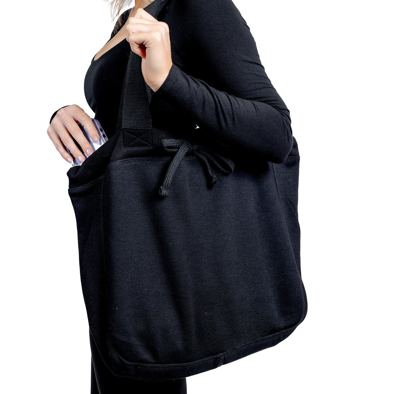 A side-view lifestyle photograph of a woman carrying a large "Black Beauty" fabric tote bag from The Branded Salon on her shoulder, reaching inside to store or retrieve her smartphone against a plain background.