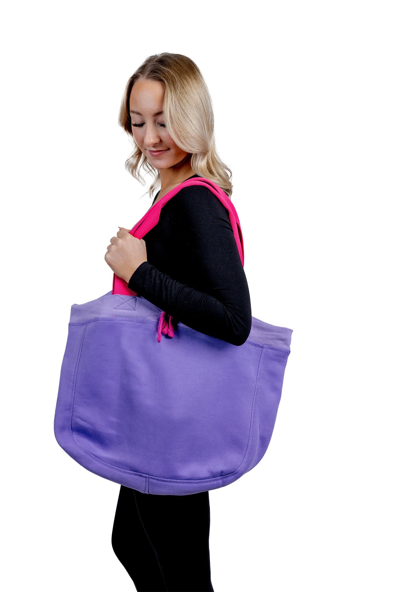 A side-view lifestyle photograph of a woman carrying a large, vibrant purple fabric tote bag with bright pink shoulder straps against a plain white background.